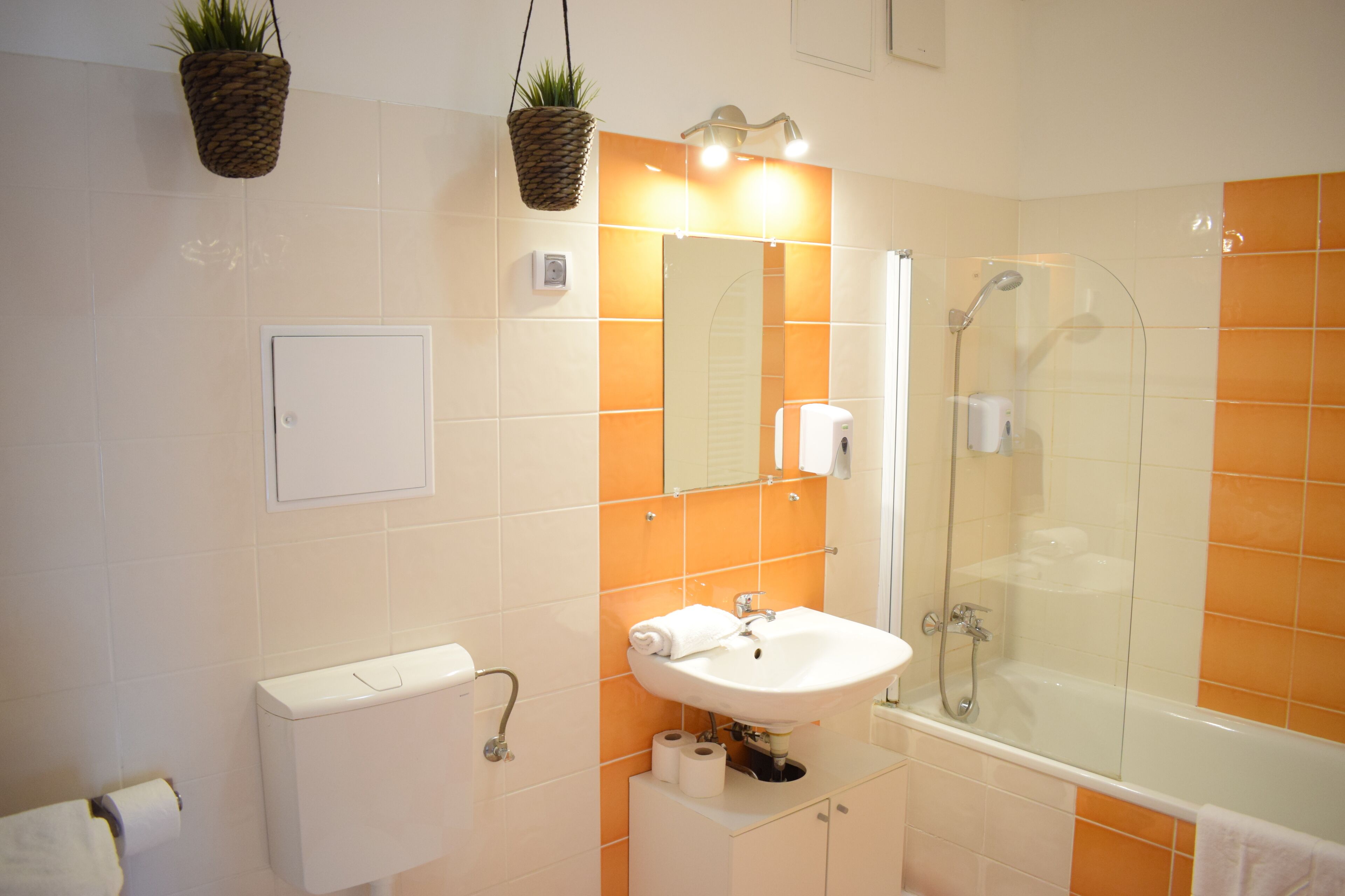 Un baño con un lavamanos blanco, cabina de ducha de vidrio y azulejos naranjas.