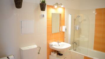 Un baño con un lavamanos blanco, cabina de ducha de vidrio y azulejos naranjas.