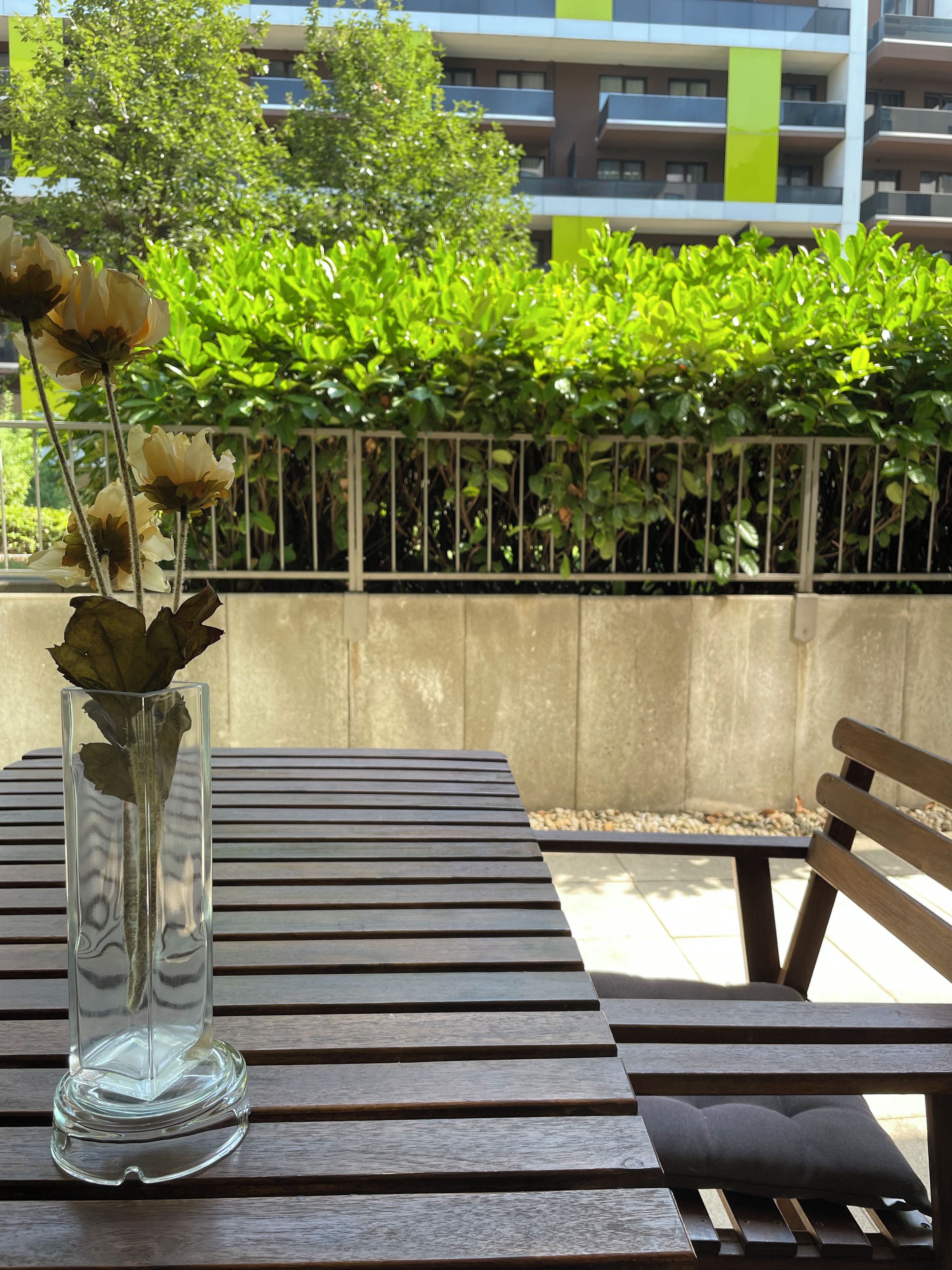 A clear glass vase with flowers on a wooden table outdoors.
