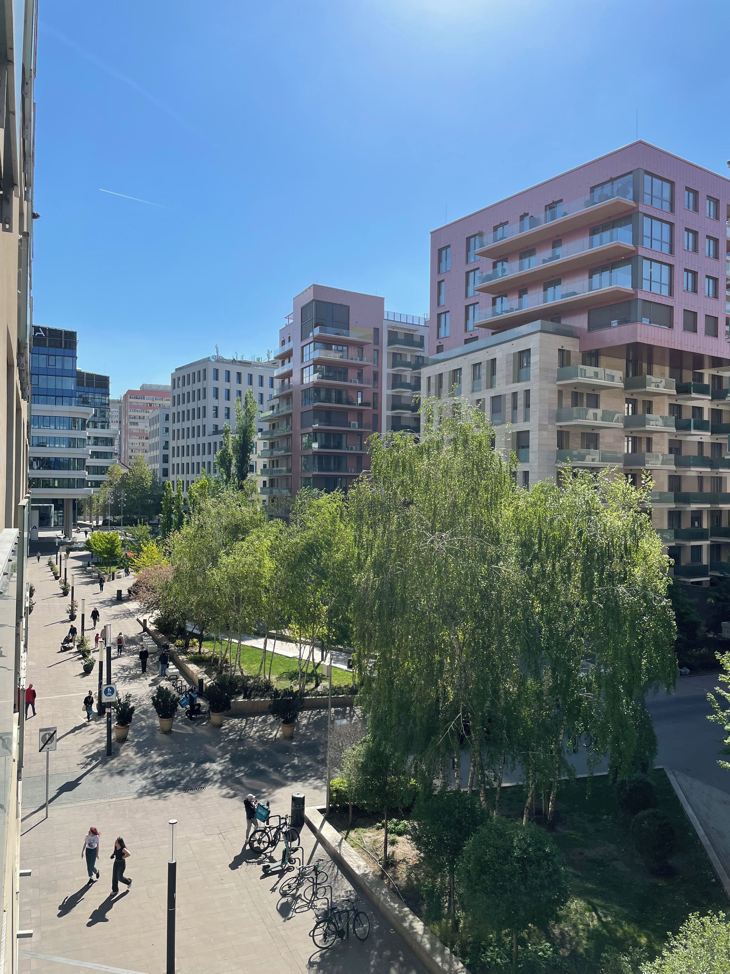 A multi-story residential building with balconies, a pedestrian walkway, and trees.