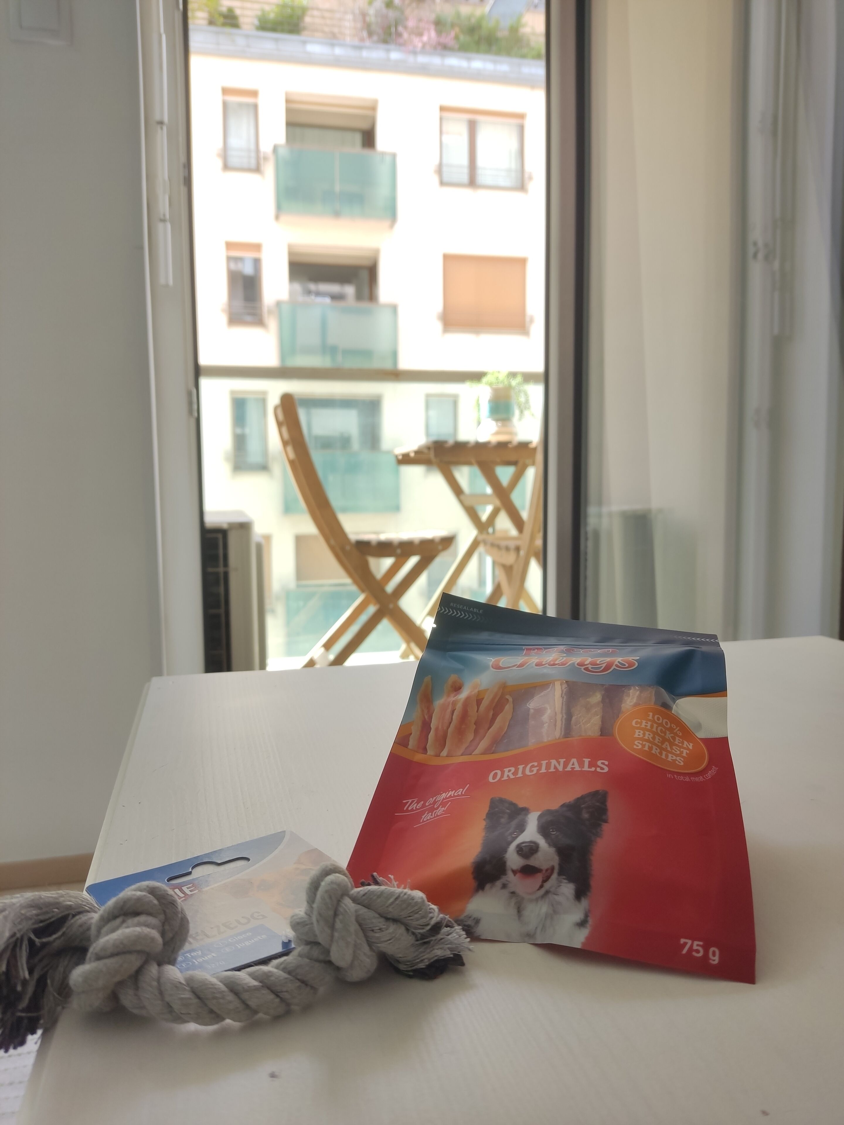 A package of Original's chicken breast strips on a table with a rope and a window view of a building.