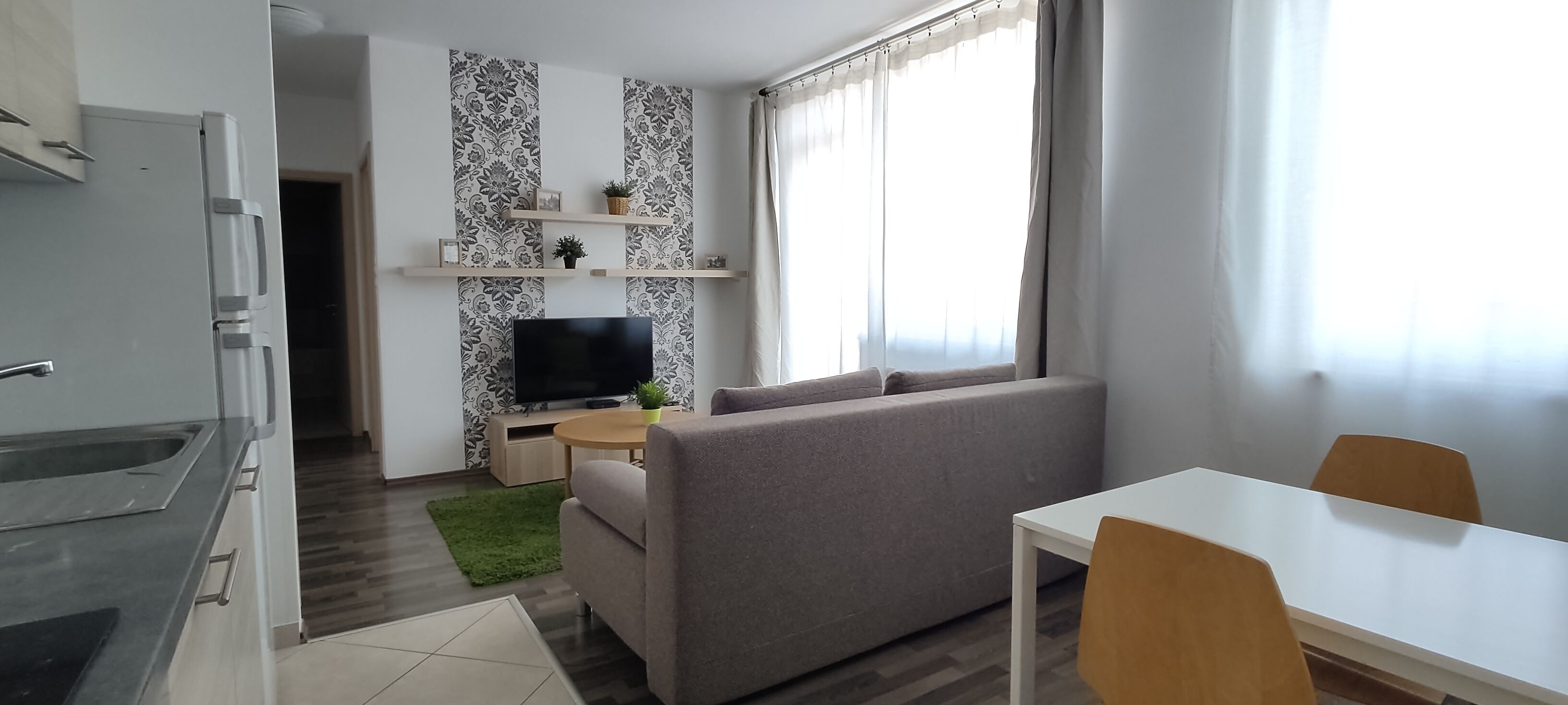 Un salon moderne avec un canapé gris, un téléviseur, une petite table et un coin repas.
