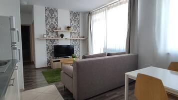 Un salon moderne avec un canapé gris, un téléviseur, une petite table et un coin repas.