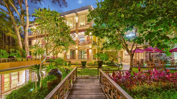 A multi-story hotel with a wooden bridge leading to a pool area, surrounded by lush greenery and outdoor seating. - Labak River Hotel by EPS (Ubud)