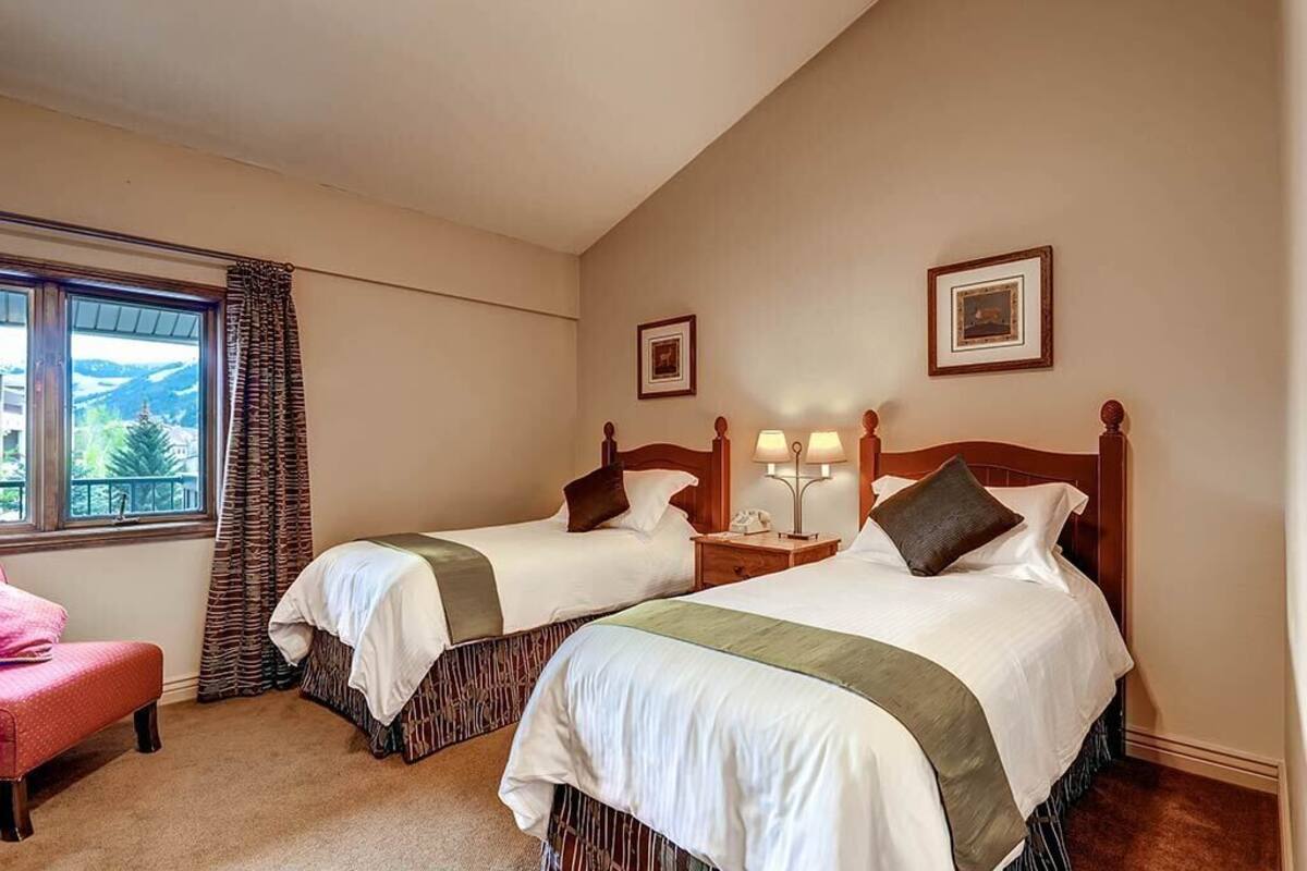 A hotel room with two beds, a window with a view, a chair, and a framed picture on the wall.