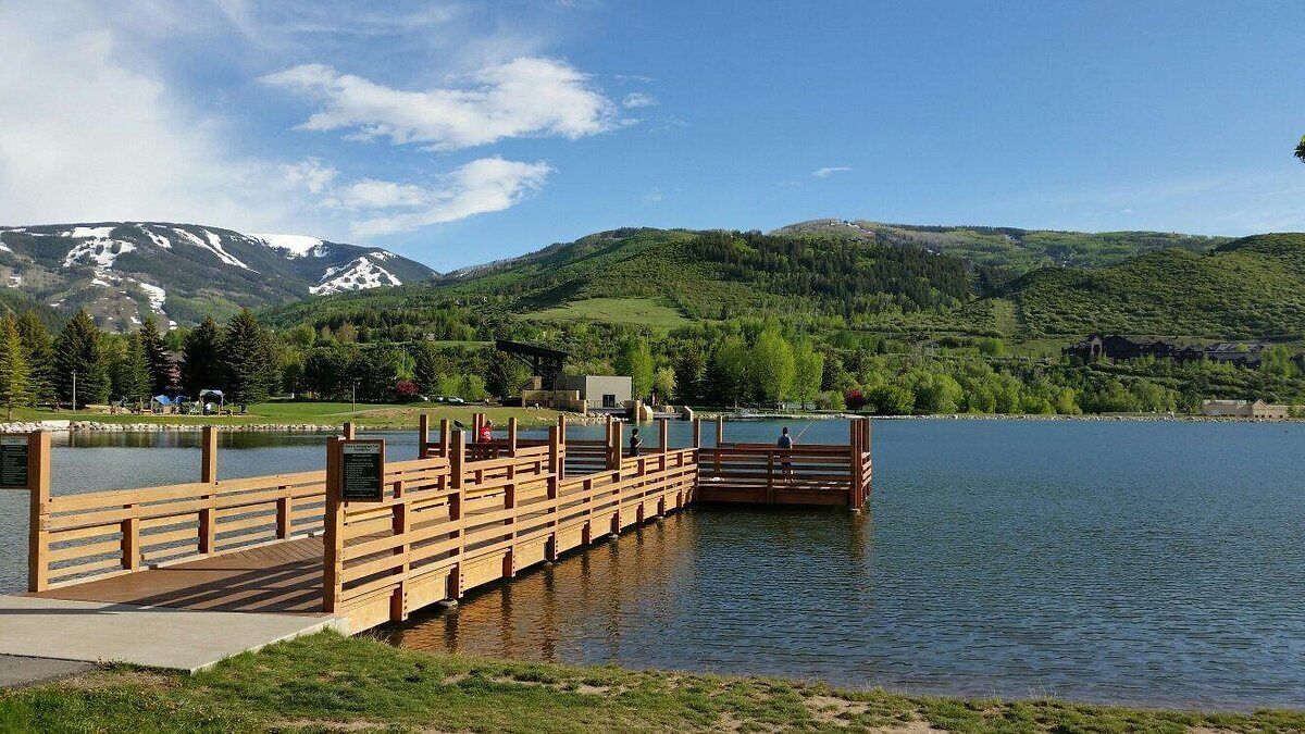 A wooden dock extending into a calm lake with a backdrop of green hills and a clear sky.