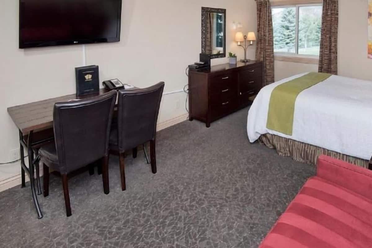 A hotel room with a bed, a desk with a chair, a TV, a dresser, and a window with curtains.