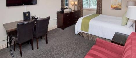 Ein Hotelzimmer mit Bett, Schreibtisch mit Stuhl, Fernseher, Kommode und einem Fenster mit Vorhängen.