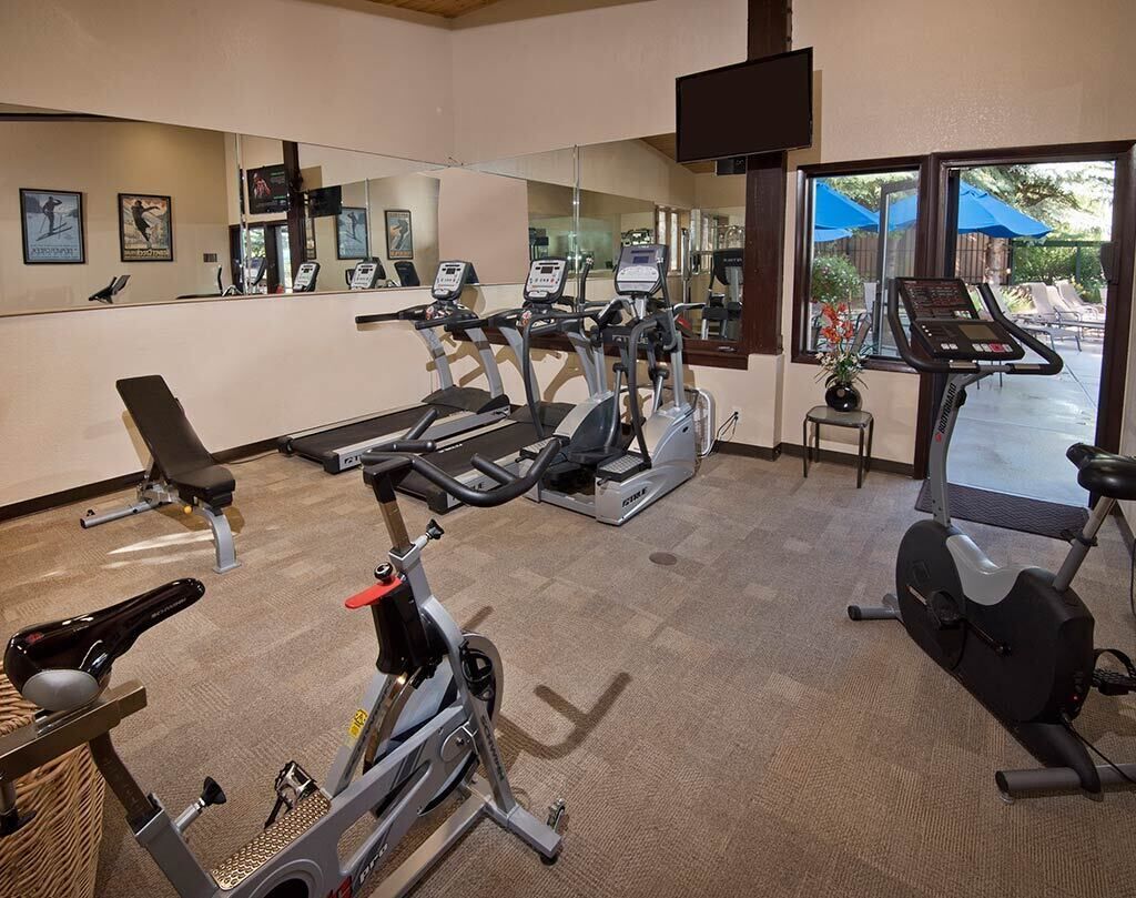 A gym with cardio machines, a bench, and a mirror.