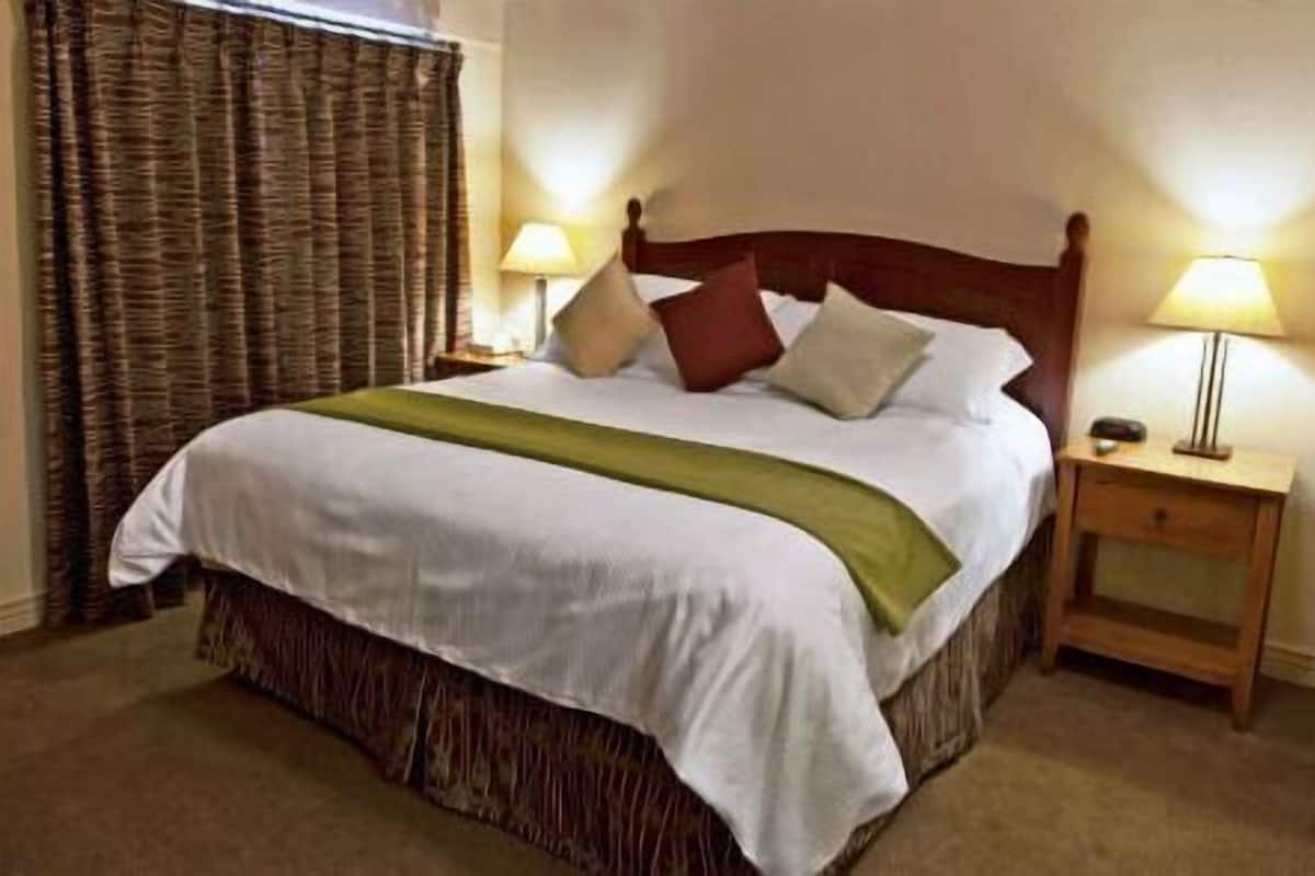 A neatly made bed with a green throw, two bedside lamps, and a wooden nightstand.