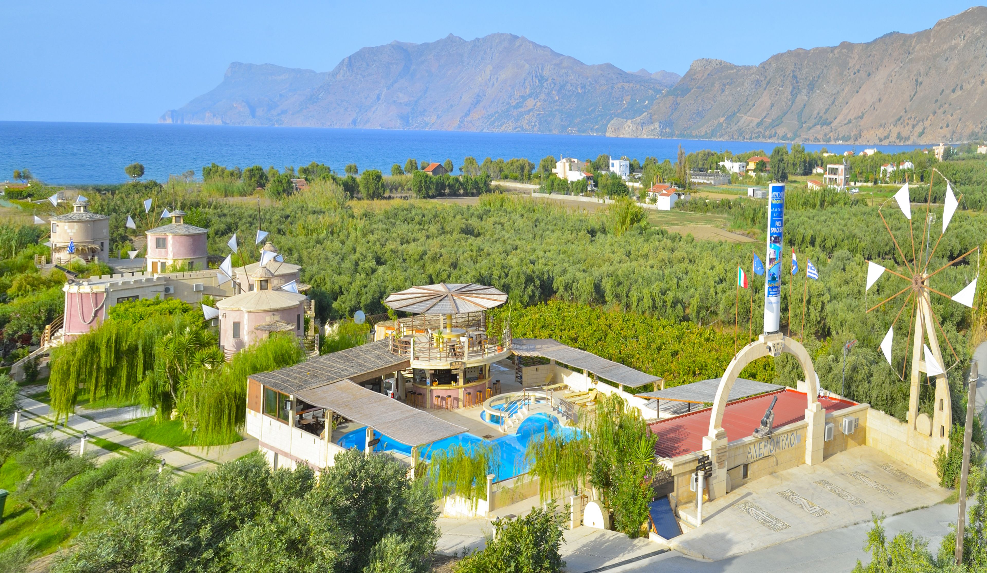 Un resort con piscina, mobiliario exterior y vistas al mar y a las montañas.
