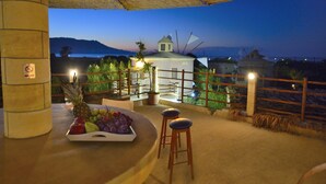 A terrace with a table set for dining, a view of the sea, and a windmill in the background. - Anemomili Village (Kissamos)