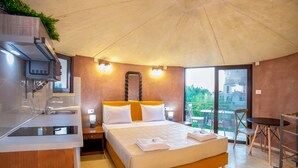 A modern hotel room with a bed, a small kitchen area, a balcony, and a view of the city. - Anemomili Village (Kissamos)