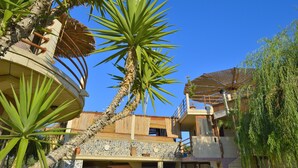 A multi-story building with a stone facade, balconies, and a palm tree in the foreground. - Anemomili Village (Kissamos)