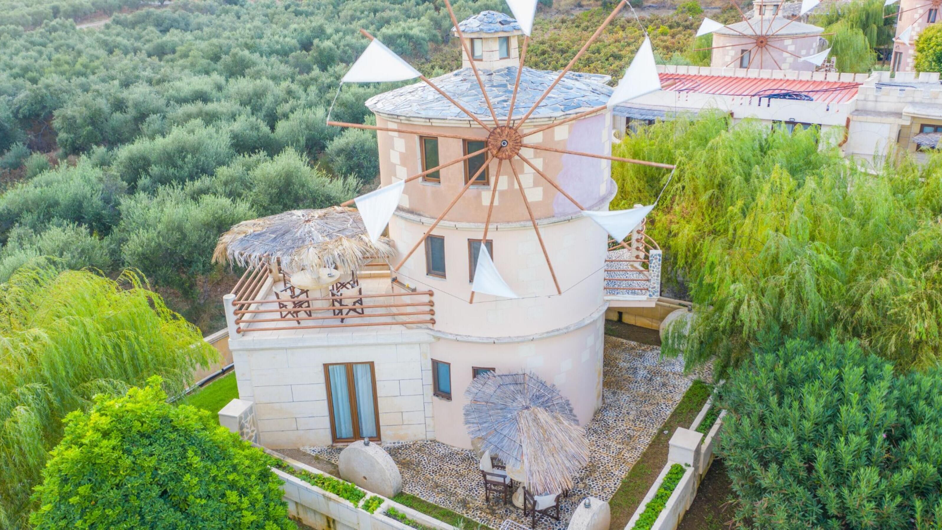 Un moulin à vent doté d’un toit de chaume, entouré d’une végétation luxuriante, et un bâtiment avec un toit en tuiles.