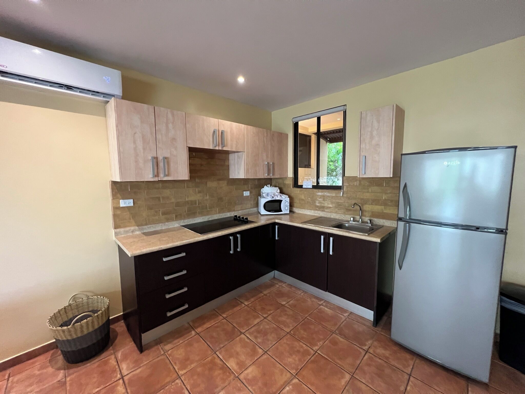 Una cocina compacta con microondas integrado, lavamanos de acero inoxidable y refrigerador de dos puertas.