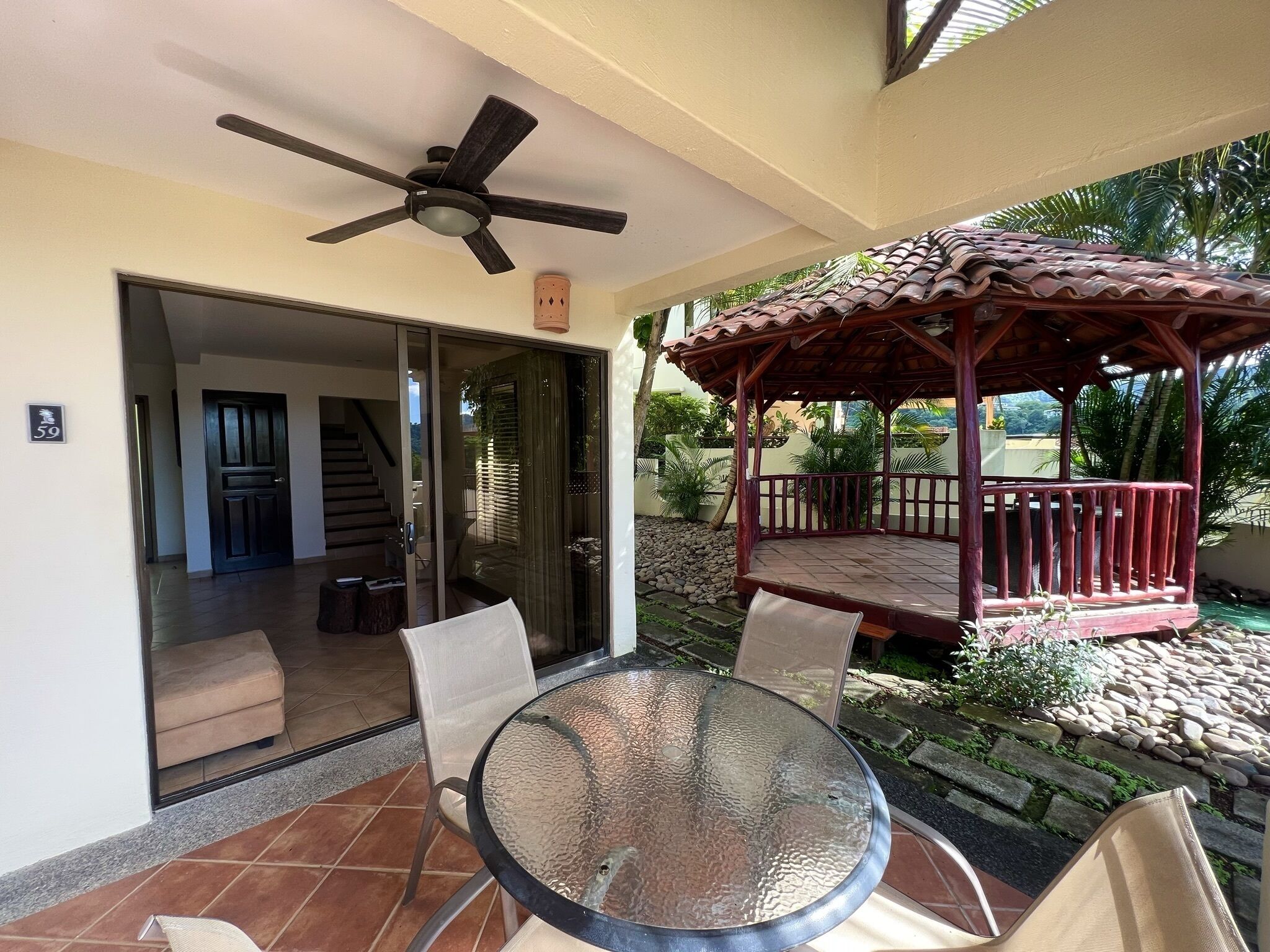 Une terrasse couverte avec une table et des chaises en verre, un ventilateur de plafond et un gazebo en bois.