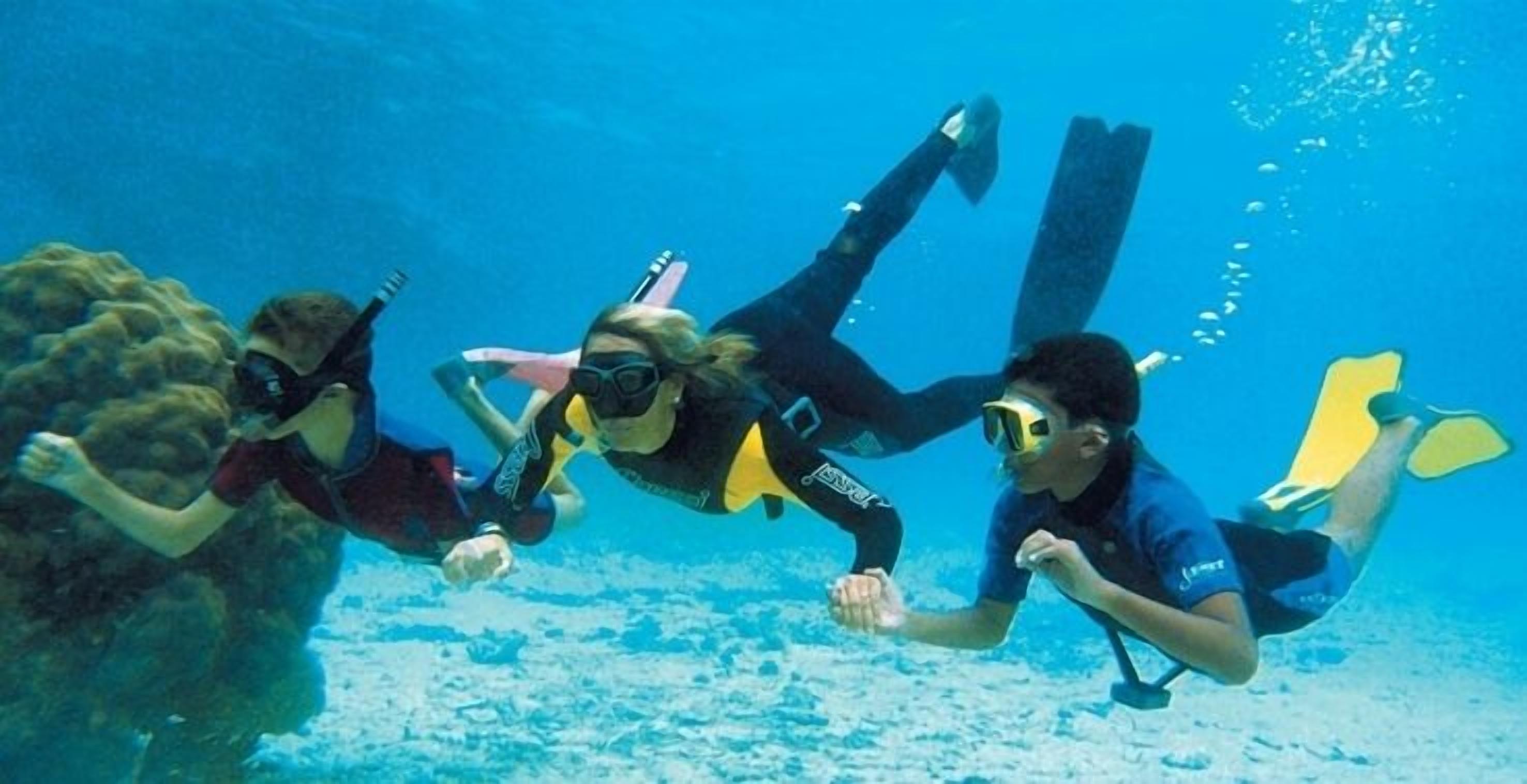 Three divers underwater with fins and masks.