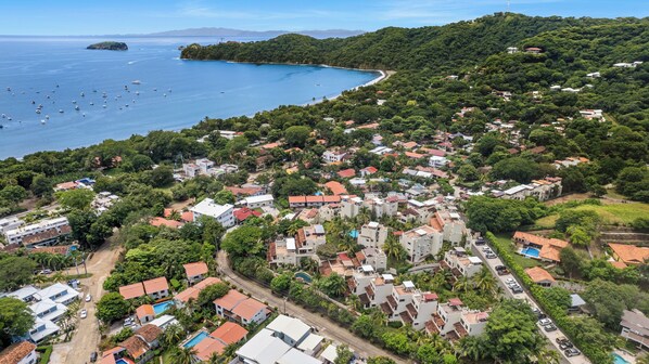 Vue aérienne d’une ville côtière, avec un mélange de bâtiments résidentiels, une plage et des bateaux sur l’eau.
