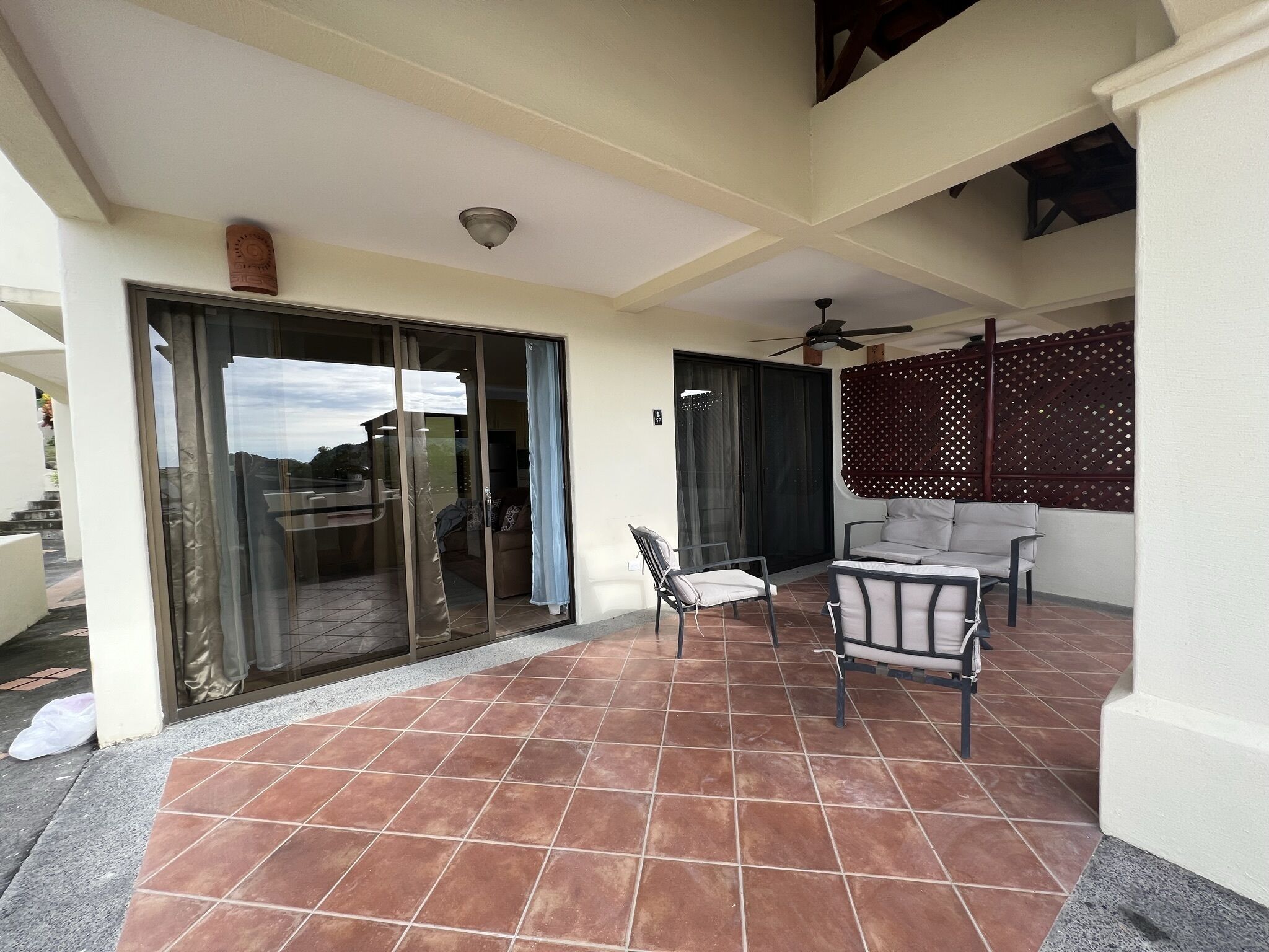 A covered patio area with tiled flooring, a sliding glass door, and two chairs.
