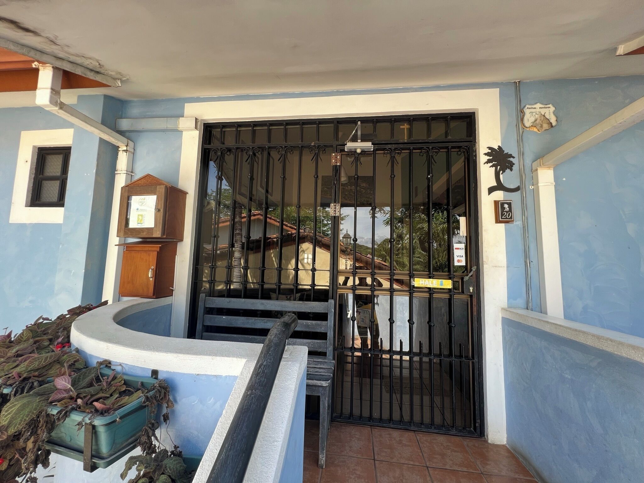 A gated entrance with a metal gate, a small wooden cabinet, and a sign indicating payment methods.