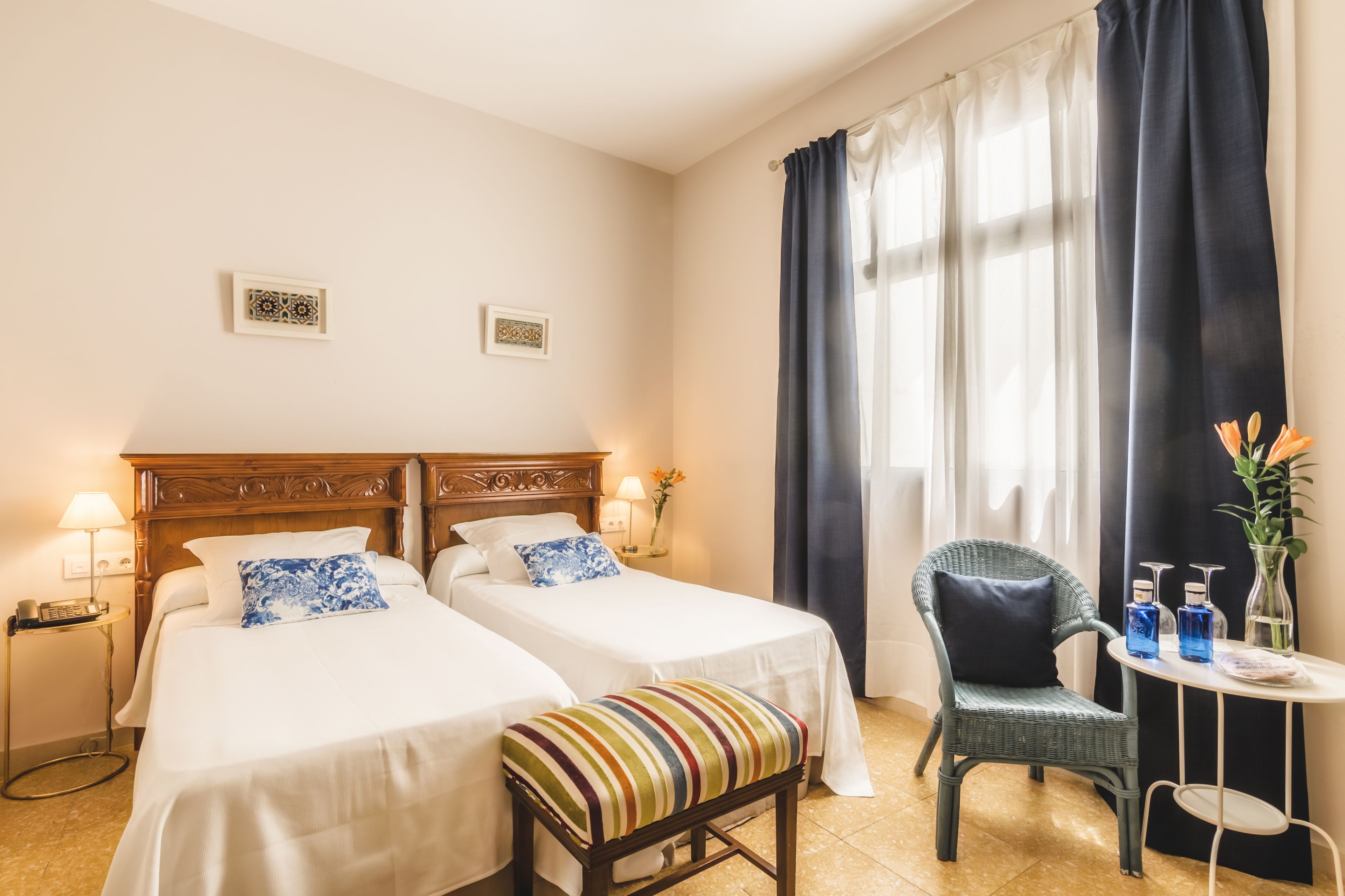 Una habitación de hotel con dos camas, una silla, una mesita pequeña con artículos de aseo y una ventana con cortinas.