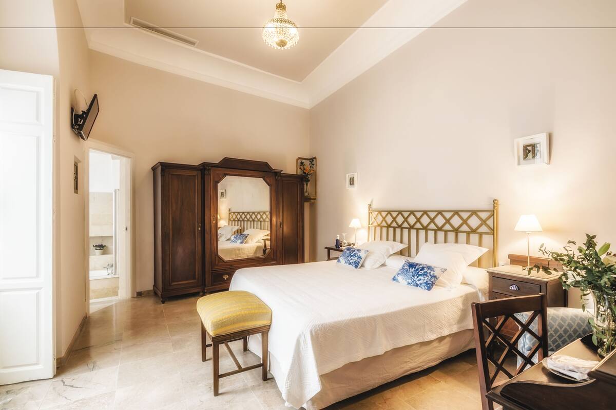 Ein Schlafzimmer mit einem großen Bett, einem Holzschrank, einer Bank, einem Schreibtisch und einer Chandelüster.