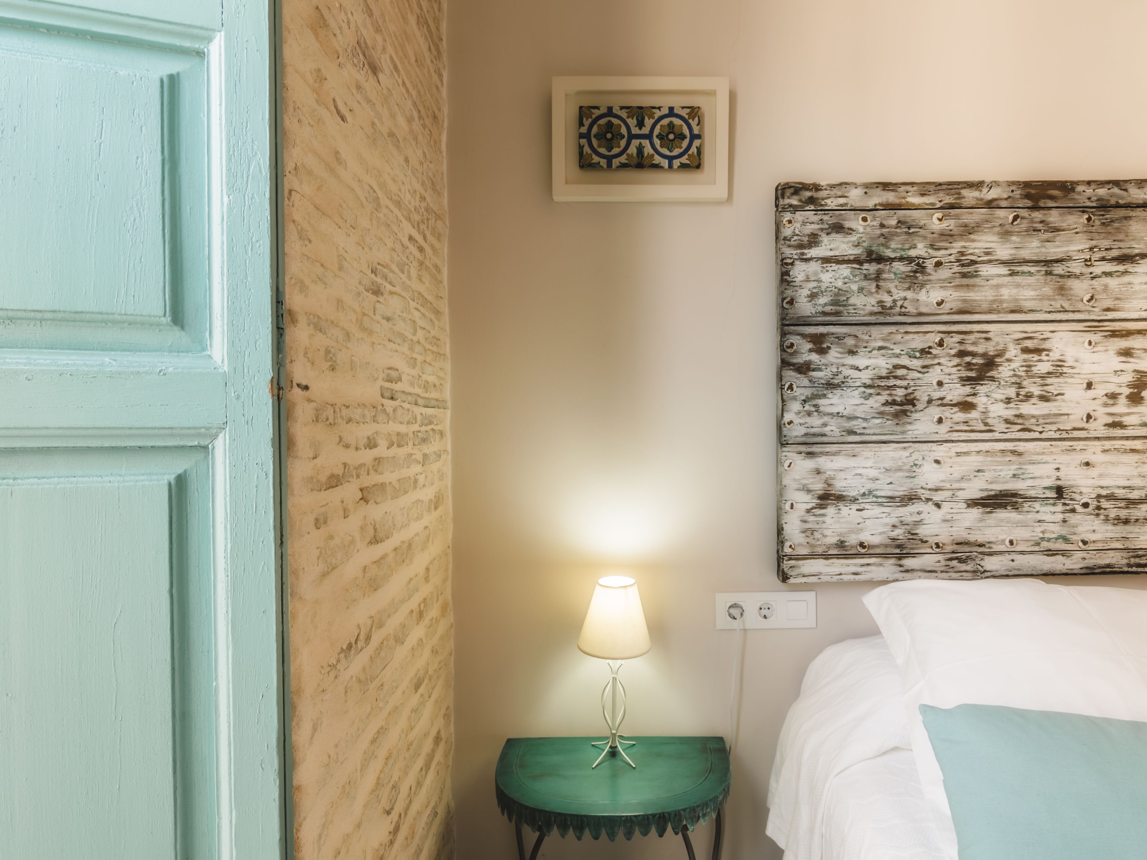 Una habitación con pared de ladrillo, cabecera de madera, mesita de noche con lámpara y cama con ropa de cama blanca.