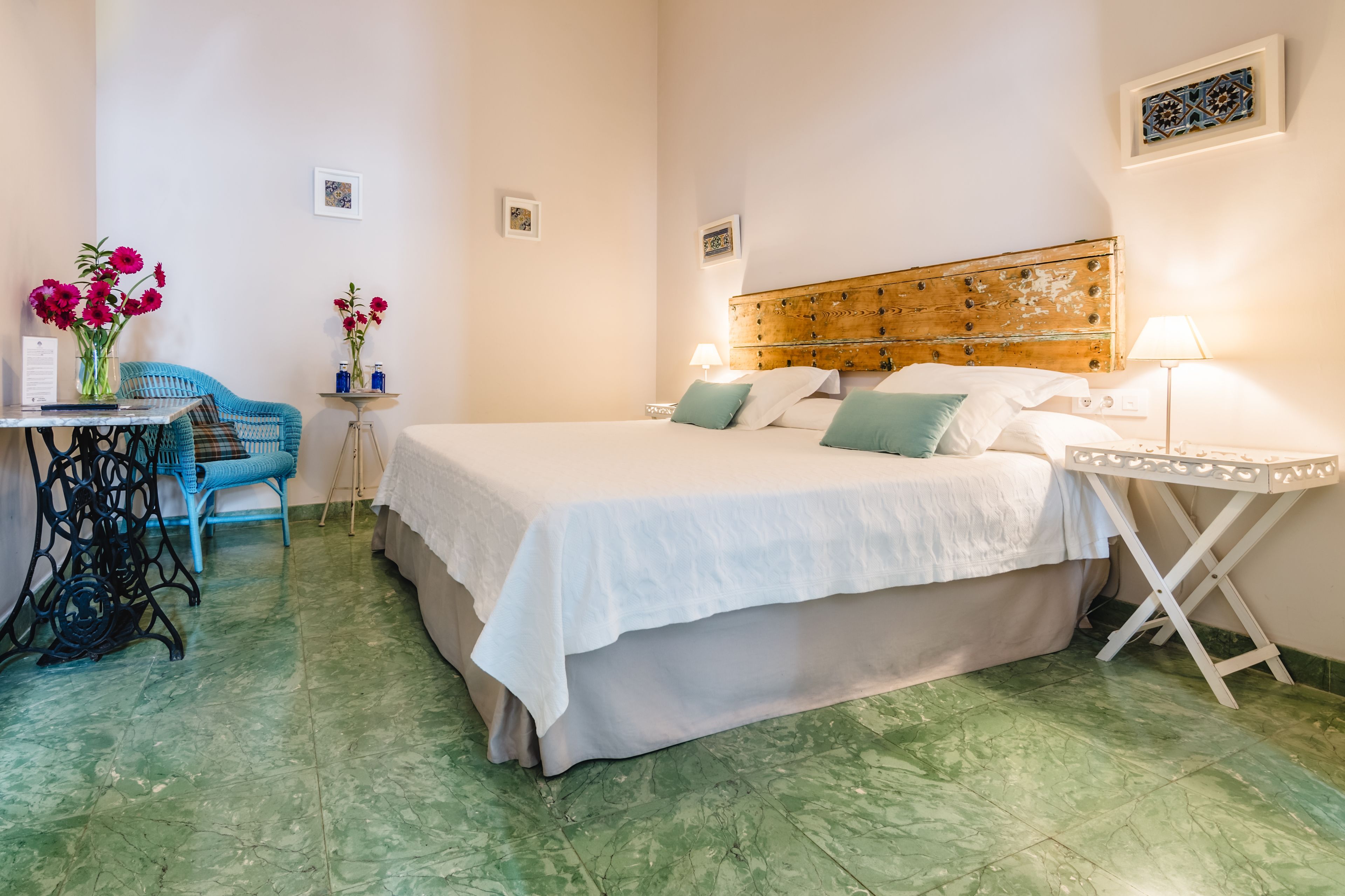 Un dormitorio ordenado con cama, mesitas de noche, una silla y una pequeña mesa con flores.