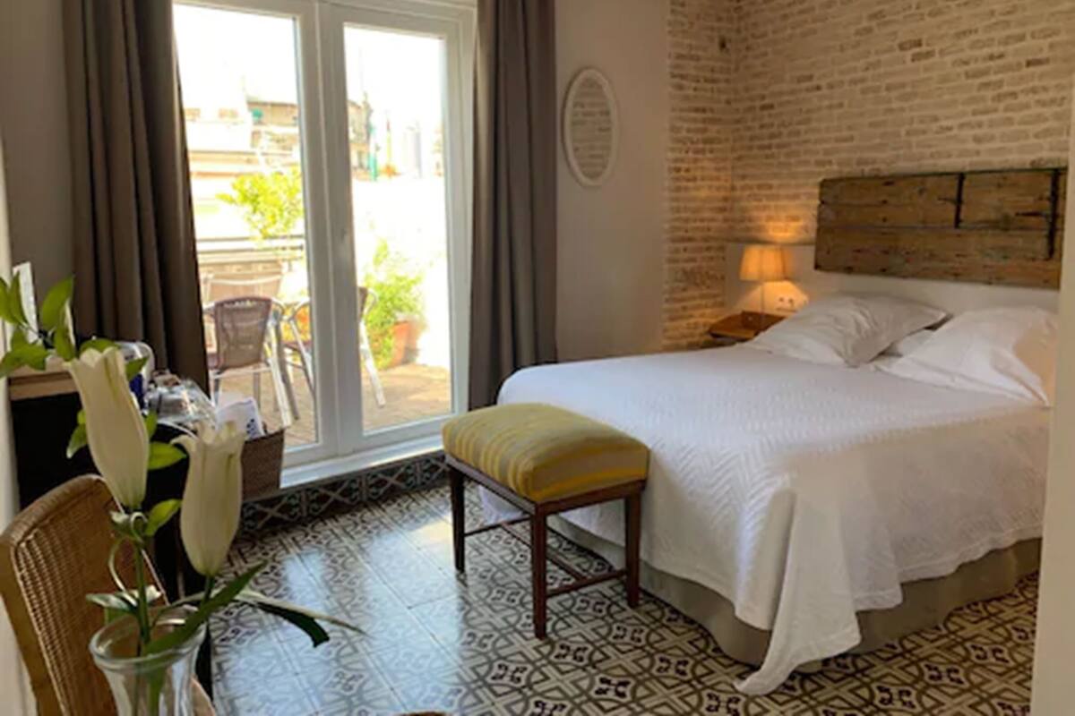 Ein Schlafzimmer mit einem Bett, einer Bank, einem Schreibtisch mit Blumen und Blick nach draußen durch eine Schiebetür.