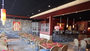 A restaurant with wicker chairs and tables, a stone wall, and a bar area with bottles.