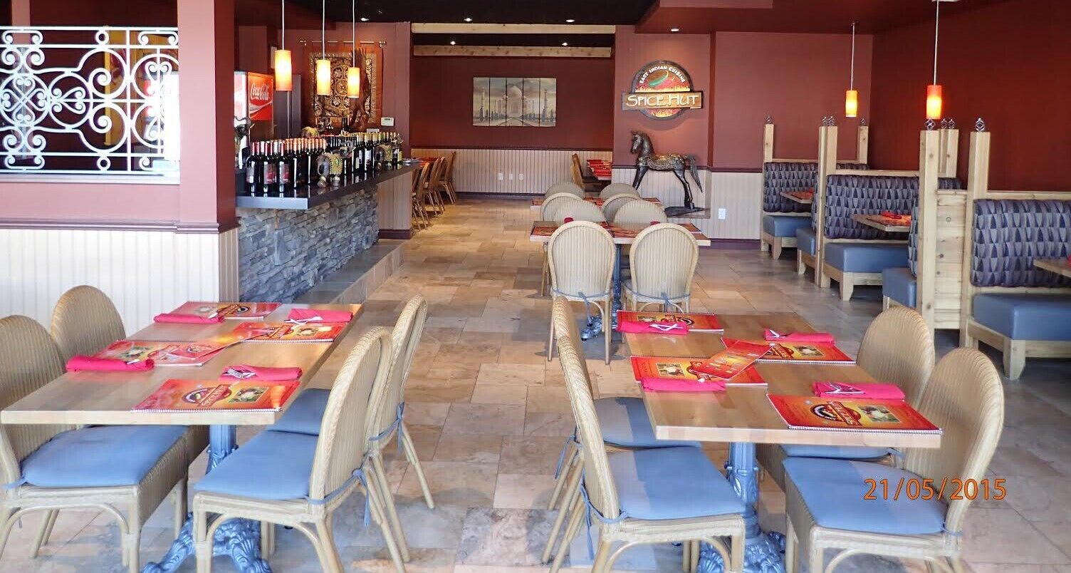 A restaurant interior with tables set for dining, a bar area with bottles, and a sign for Spice Hut.