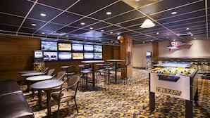 A billiards room with multiple tables, a foosball table, and a large screen displaying sports.