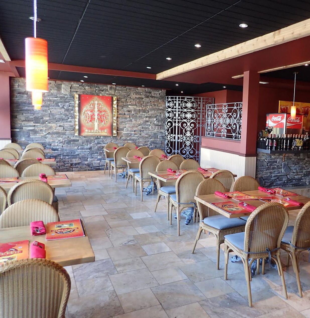 A restaurant with wicker chairs and tables, stone walls, and a Coca-Cola refrigerator.
