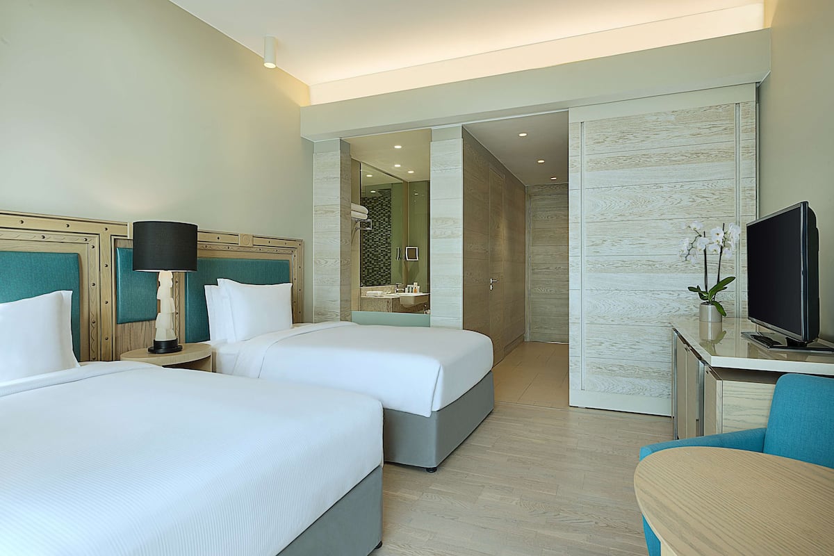 A hotel room with two beds, a desk with a TV, and a bathroom visible through an open door.
