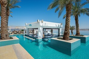 A modern pool area with a bar, lounge chairs, and palm trees. - Hilton Dead Sea Resort & Spa (Sweimeh)
