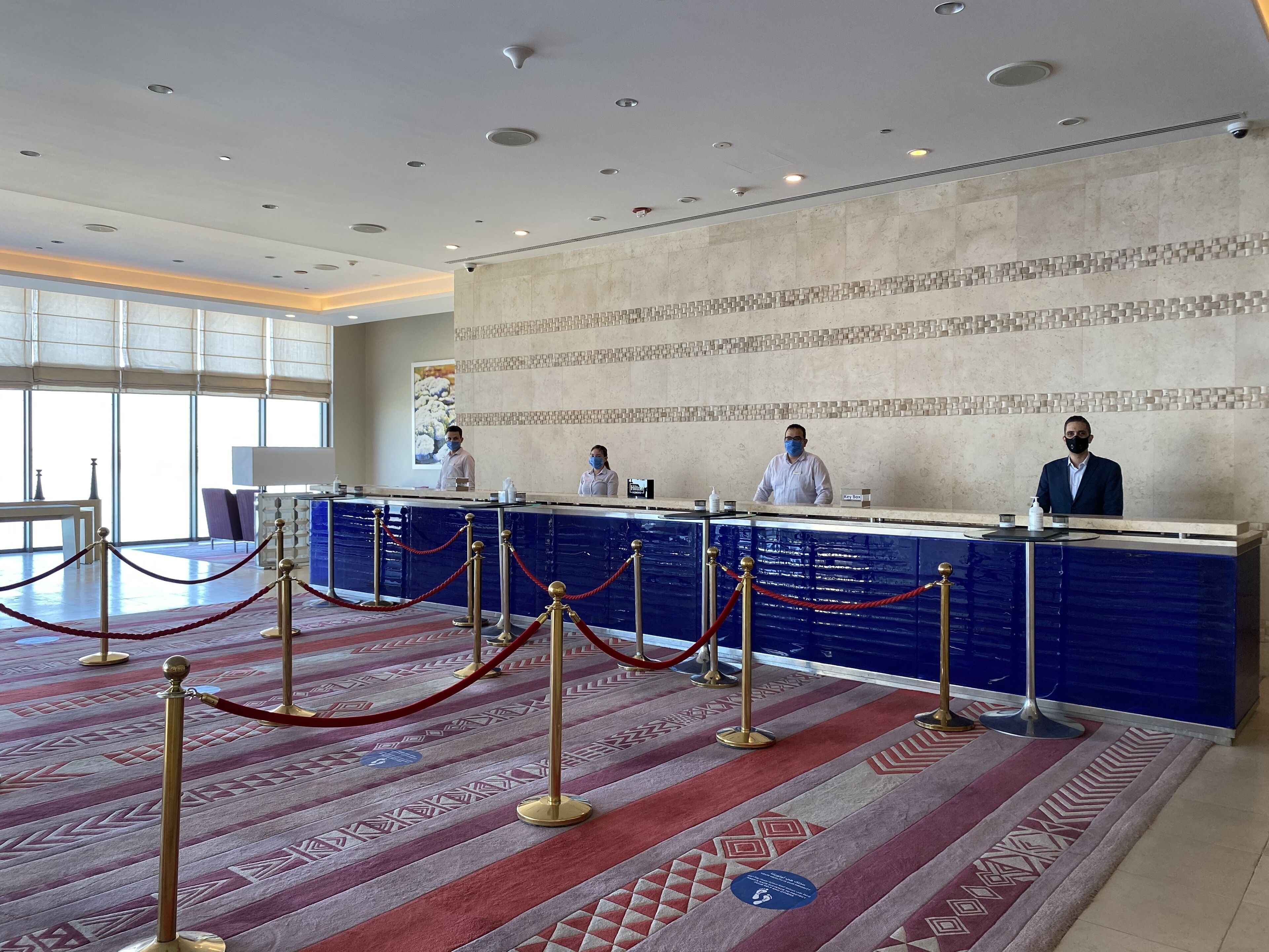 A hotel reception area with a blue counter, staff behind it, and a patterned carpet.