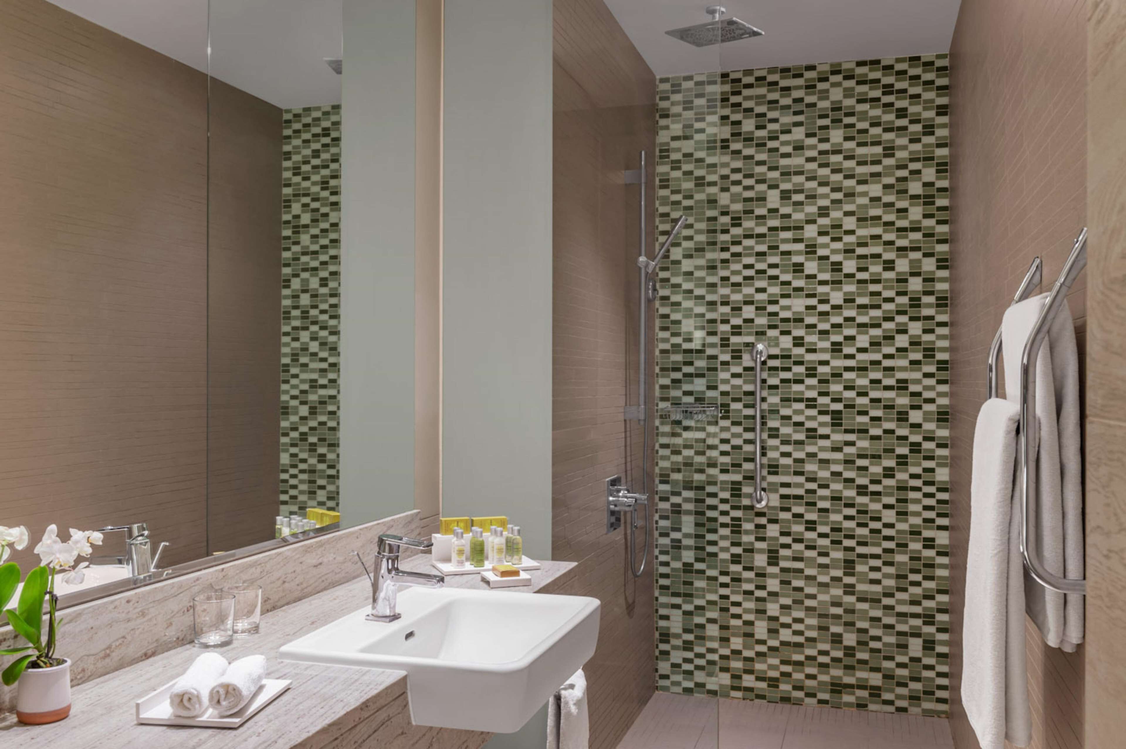 A modern bathroom with a large mirror, a sink, and a shower area.