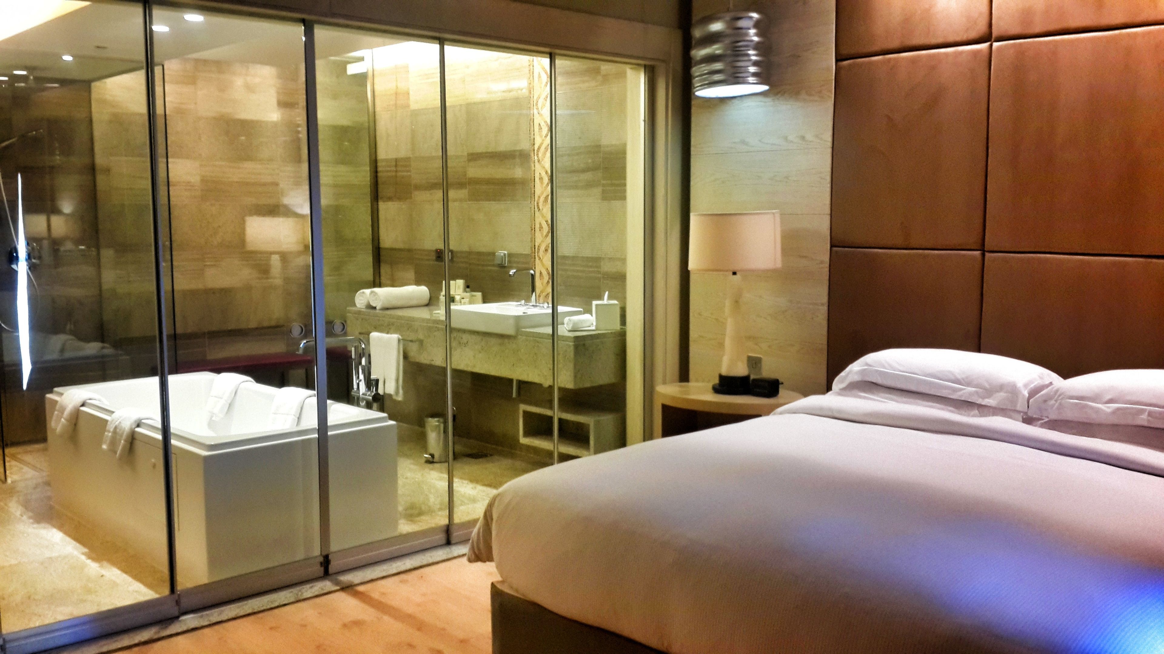 Una habitación de hotel moderna con ducha de vidrio, una cama grande y una mesita de noche con lámpara.