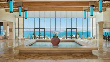 A spacious lobby with a large pool, seating area, and a view of the sea.
