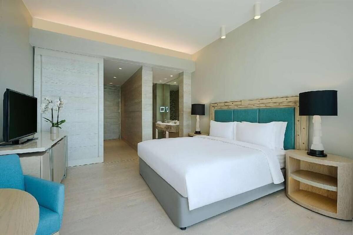 A modern hotel room with a bed, a TV, a desk, and a bathroom visible through an open door.