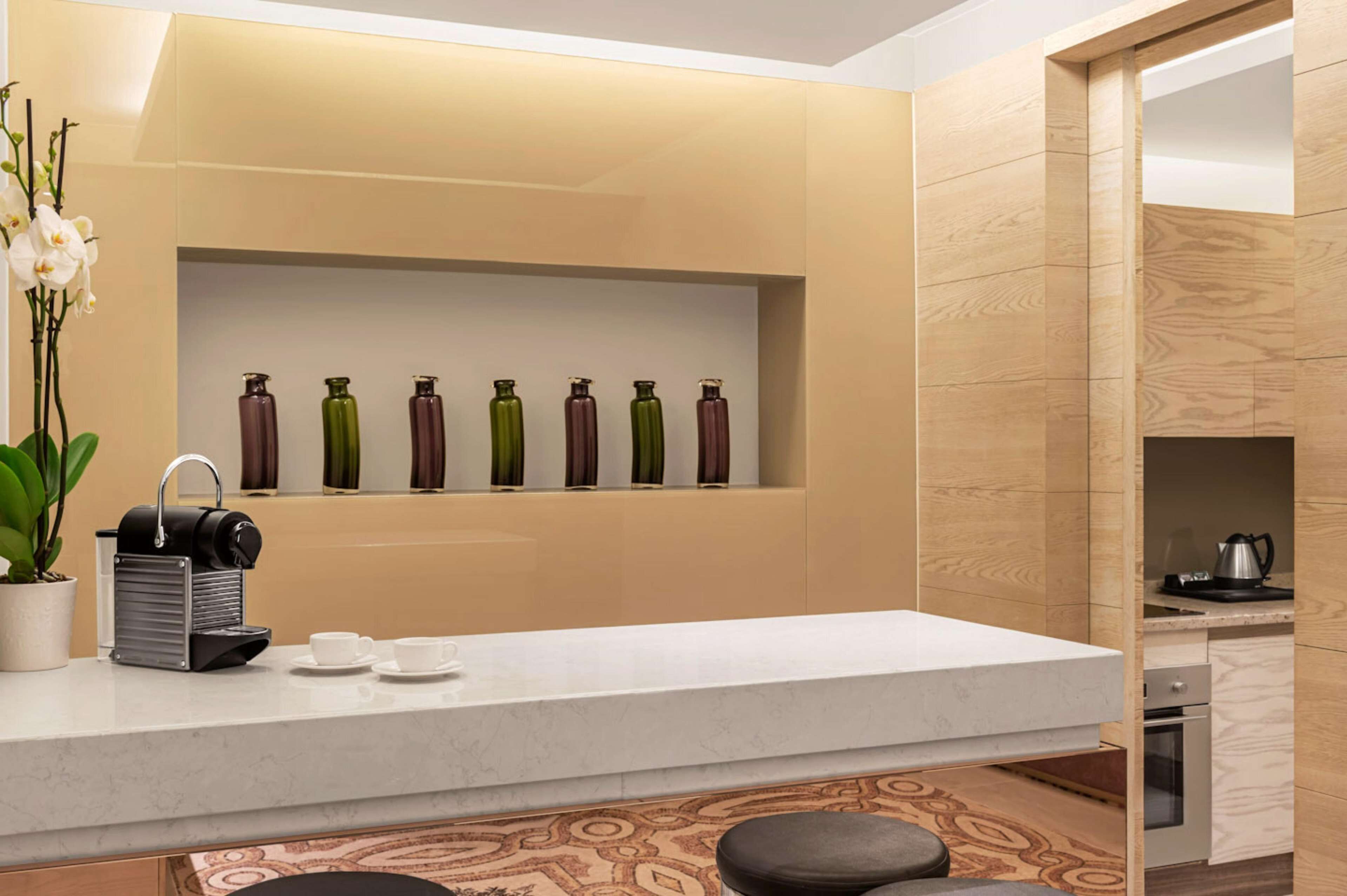 A modern kitchen with a marble countertop, a coffee machine, and a shelf with decorative bottles.