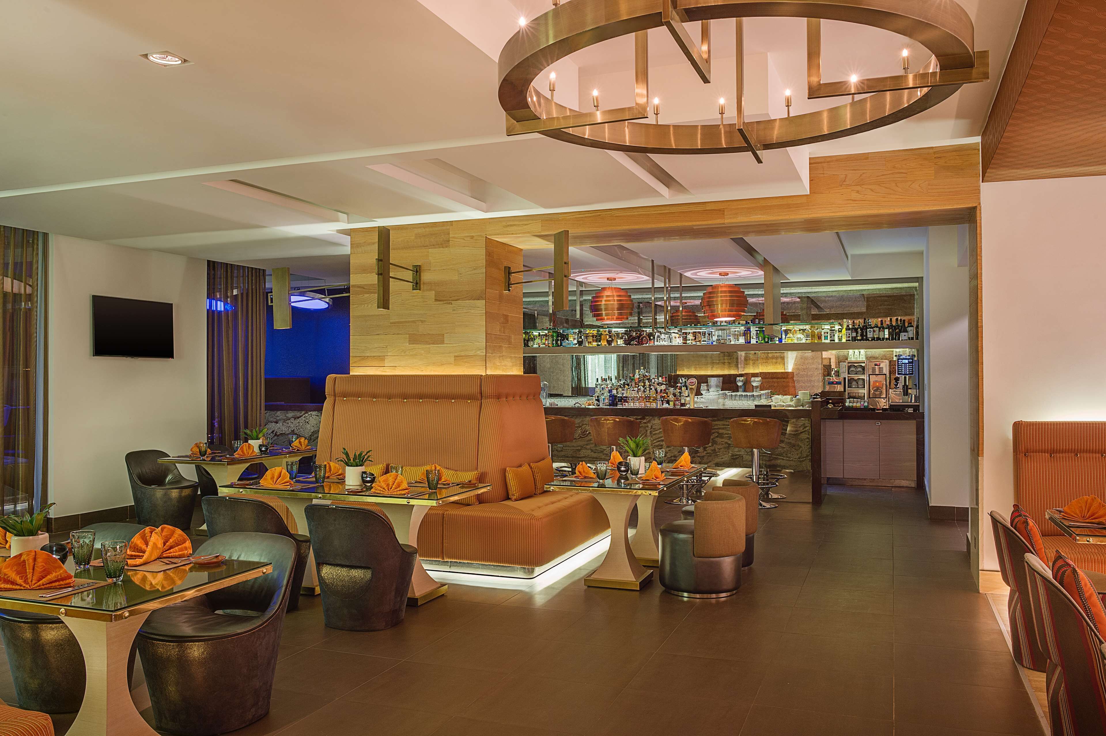 A modern bar area with a bar counter, seating, and a television screen.