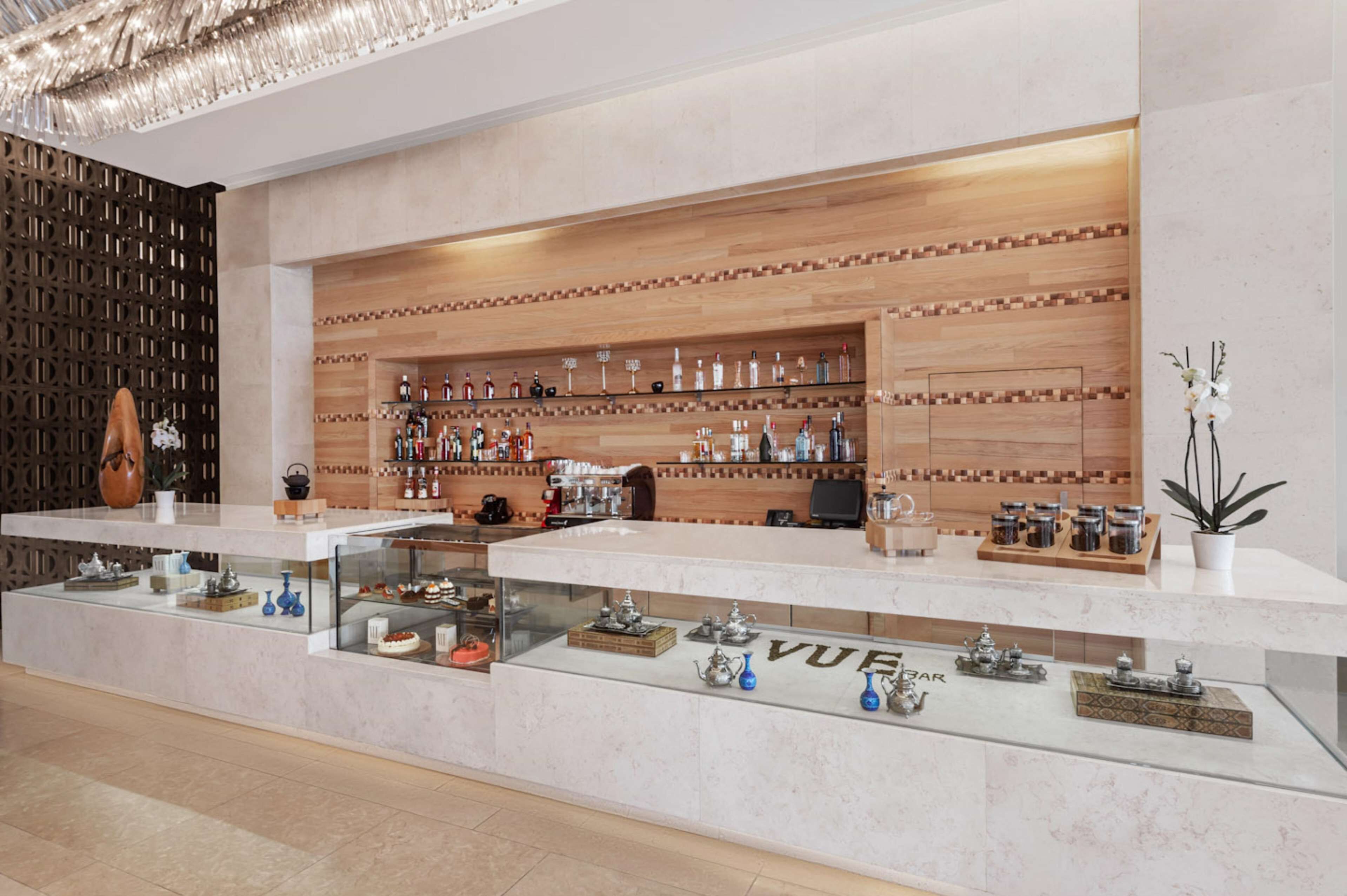 A modern bar area with a wooden wall and shelves displaying bottles and glassware.