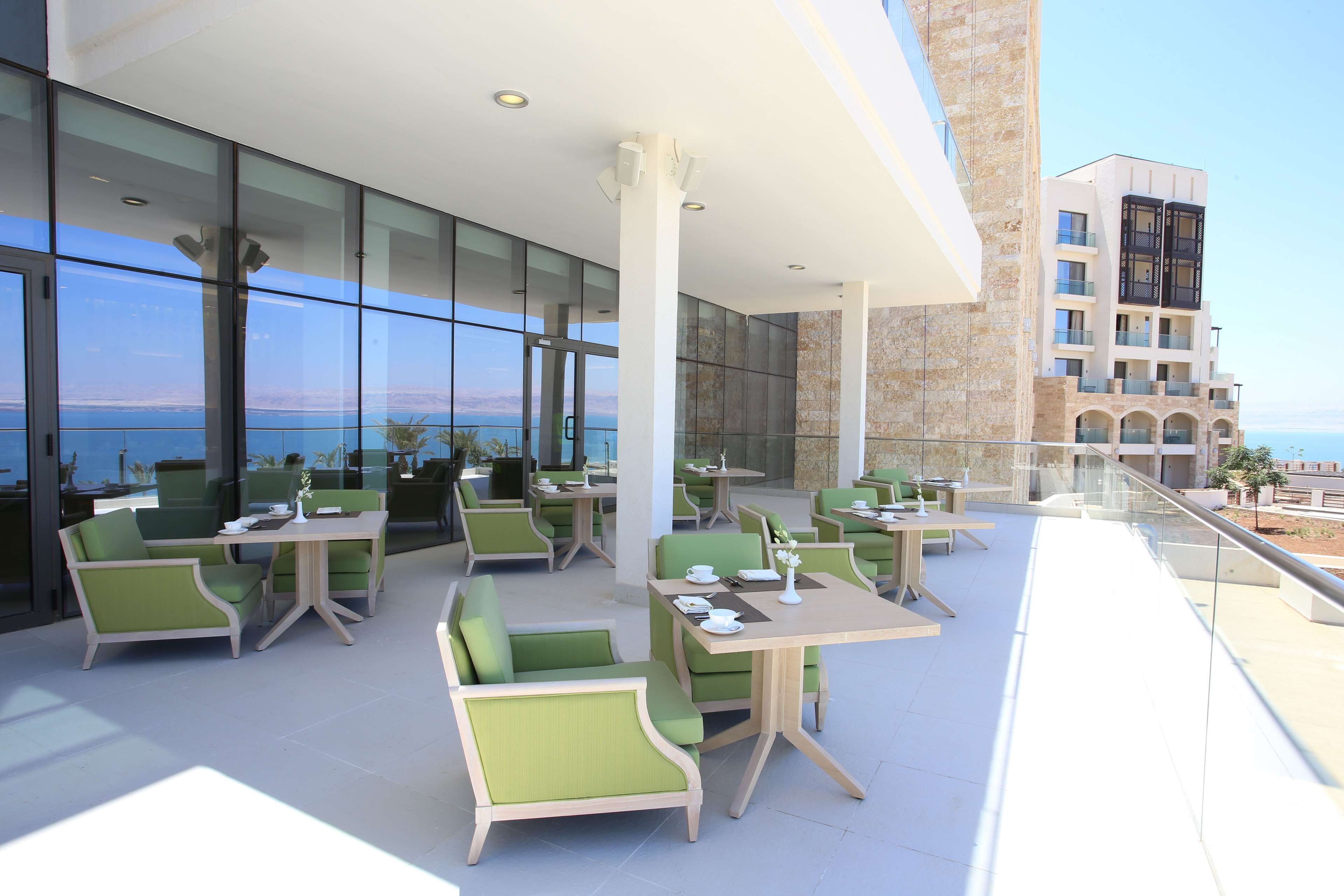 Un área de comedor en la azotea con paredes de vidrio, asientos al aire libre y vista al mar.