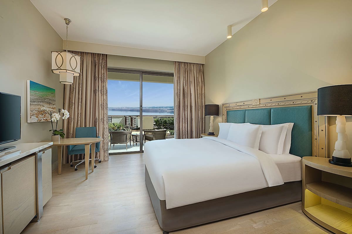 A hotel room with a large bed, a desk with a chair, a television, and a view of the outdoors.