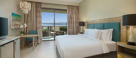 A hotel room with a large bed, a desk with a chair, a television, and a view of the outdoors.