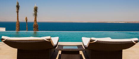 Uma área à beira da piscina com espreguiçadeiras e vista para o mar.