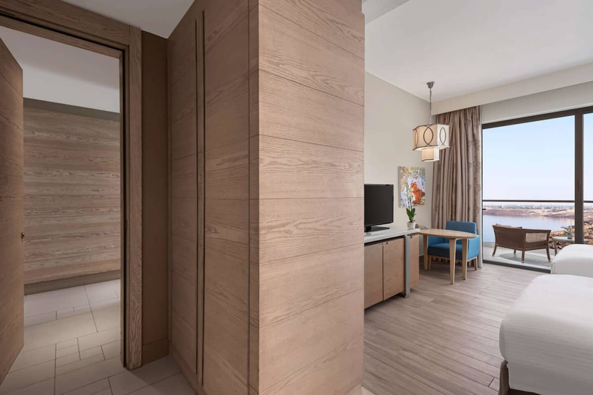 A modern hotel room with a large window, a television, a desk, and a bed.