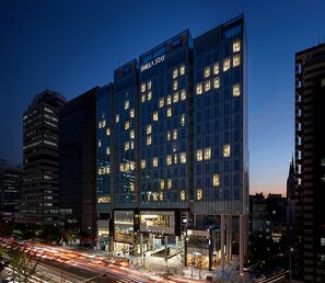 Un hotel moderno con fachada de vidrio, varios pisos y ventanas iluminadas.